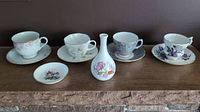 Overview of four teacups with matching saucers and small floral plate alongside bud vase with colorful floral pattern