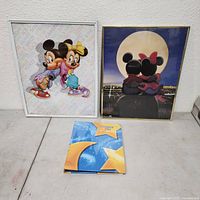 Two framed Disney posters and the Disneyland Hotel Directory booklet on a flat surface.