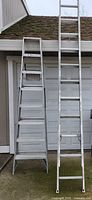 White 8 ft step ladder by Keller next to a white extension ladder leaning against a garage door, showing relative sizes and ladder condition.
