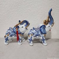 Pair of blue, white, and gold porcelain elephant figurines with musical instruments side view.