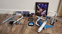 Wide shot showing multiple metal model airplanes of various airlines and colors, a book 'The Triumph of Flight', and aviation memorabilia on wooden floor.