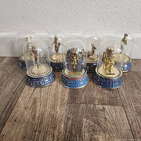 Seven vintage Franklin Mint Egyptian statues under glass domes with blue hieroglyphic bases, arranged on wooden floor.