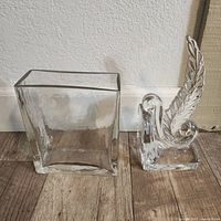 Front and side view of a clear glass rectangular vase and a bookend shaped like a bird with feather.
