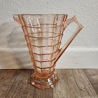 Front angle view of the pink depression glass pitcher showing the stepped geometric body, angular handle, and octagonal base with felt pads.