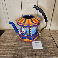 Front and side view of a carousel-themed teapot showing spinning horse figurines and colorful painted details with black handle