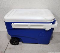 Blue and white Igloo cooler with lid closed and side wheels visible.