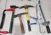 Photo showing a collection of hand tools on a white surface. Includes 3 hammers, a hacksaw, a caulking gun with a tube, and a torque wrench.