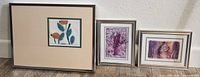 Set of three small framed art pieces together against wall on wood floor.
