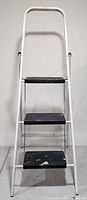 Front view of the white metal 3-step ladder showing black steps and paint wear.