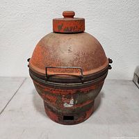 Front view of vintage ceramic Imperial Kamado grill with dome lid, showing worn orange paint and metal latch handles.