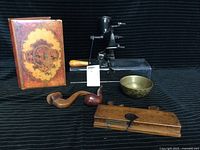 Photo showing entire lot including coffee grinder, brass bowl, wooden planer, two pipes, and wood box displayed on black fabric
