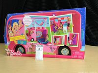Barbie camper van packaging box front showing vibrant pink camper and images of the play features including a pop-up 2nd story and dolls playing inside and outside the camper.