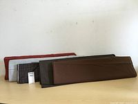 Five bolts of fine wool cloth laid flat and side by side showing colors and textures.