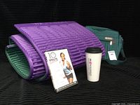 Complete lot showing the purple and green exercise mat, green Samsonite shoulder bag, exercise DVD and travel mug on a black background.