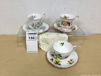 Three floral tea cups and saucers arranged with white crochet doilies in the background