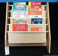 Front view of the wooden kids’ bookshelf with four beige canvas shelves holding ten children's books with visible colorful covers.