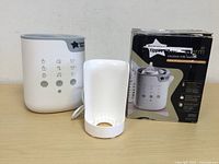 White and grey electric milk warmer unit with control buttons and original box packaging displayed on a wooden surface.