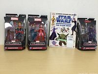 Three Marvel Legends action figures in packaging and one Star Wars sticker collection book.
