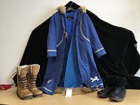 Front view of blue Yukon parka open showing felted wool lining, brown tall lace-up boots with white fleece, and black ankle boots with black fleece cuff.