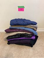 Stack of 10 folded women's puffer jackets and vests in assorted colors.