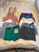 Full lot laid out on bed showing all 11 pieces including overalls, shorts, and skirts in various colors and denim styles.