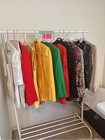 View of 13 colorful vintage women's garments hanging on a clothing rack, including jackets and skirts in colors white, red, yellow, green, floral, and polka dots.