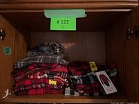 13 folded plaid and flannel shirts stacked inside a wooden cabinet shelf, showing various patterns mainly in red, black and grey.