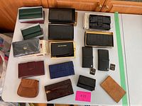 All wallets and organizers laid out on white table, various colors and brands, some in boxes and plastic packaging.