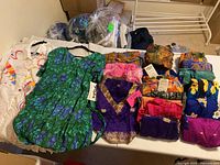 Overview of lot showing 18 pieces of vibrant batik summer clothing in bags and folded on table, including colorful dresses and tops.