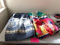 Five knit wool sweater and vest pieces displayed on a table, showing two gray and white vests together and three colorful button-up sweaters with different patterns.