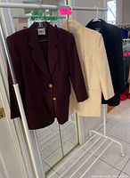 Six vintage women's suit jackets hanging on a rack, visible colors maroon, cream, navy