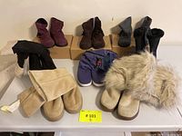 Lot of 8 pairs of women's winter boots, size 8, arranged on a table showing multiple colors and styles including purple Nike Sensory Motion System boots, black, brown, and beige fur and suede boots. Some pairs are boxed.