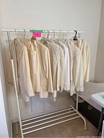 Side view of multiple cream-colored blazers and suit jackets hanging on white metal rack against a wall.