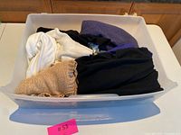 Photo of all sweaters and cardigans folded in a plastic bin, showing various colors including beige, white, purple, blue, and black knits.