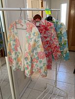 Three floral print outerwear pieces hanging on rack: cream cardigan with multicolor flowers, red floral blazer, and blue floral blazer.