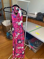 Vintage De Weese Design halter swim dress hanging on a rack next to tables and storage containers showing the full length and floral pattern.