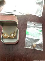 Overview of two main earrings in box and two single studs in bags on tabletop