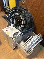Overview photo with three containers of assorted cables including large black cable coil, box of white cable, and clear container with spooled cables.