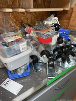 Photo showing metal casters with mounting plates, assorted screws and nails in plastic bins and containers on a workbench surface.