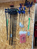 Photo shows a variety of clamps hung on a pegboard wall, largest is a 36-inch bar clamp. Also visible are hanging packages of red clamping squares.