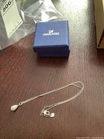 Full view of the Swarovski necklace with pendant and packaging box on wood surface.