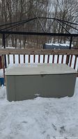 Snow-covered gray resin deck box, front view