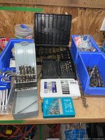 Overview of drill bits, hex keys, punches, tool cases and blue plastic bins on a wooden surface.