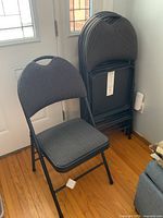 One folding chair set up showing fabric seat and back and metal frame with handle on top.