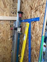 Bosch tripod stand alongside large Stabila spirit level and Empire drywall T-square mounted on OSB wall