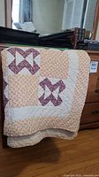 Quilt folded over a wooden dresser showing patchwork pattern and condition.