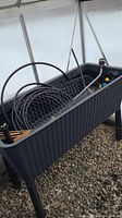 Front view of black resin raised planter containing various garden accessories