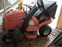 Left side view of orange Simplicity riding lawn mower showing body, deck and grass catcher