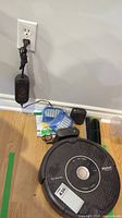 Roomba unit alongside dock, adapter, filter and brushes on hardwood floor