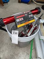 Tajima Convoy Super Sausage Gun and adhesive dispensers inside white pail on concrete floor.